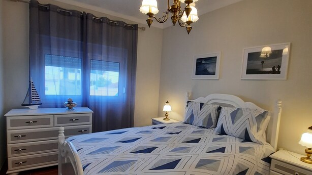 Ein Schlafzimmer mit einem Bett, einem Nachttisch, einer Kommode, einer Pendelleuchte und zwei gerahmten Bildern an der Wand.