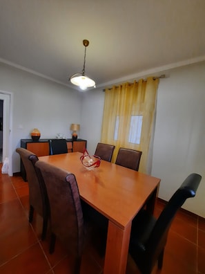 A dining area with a wooden table and chairs, a hanging light fixture, and a yellow curtain.
