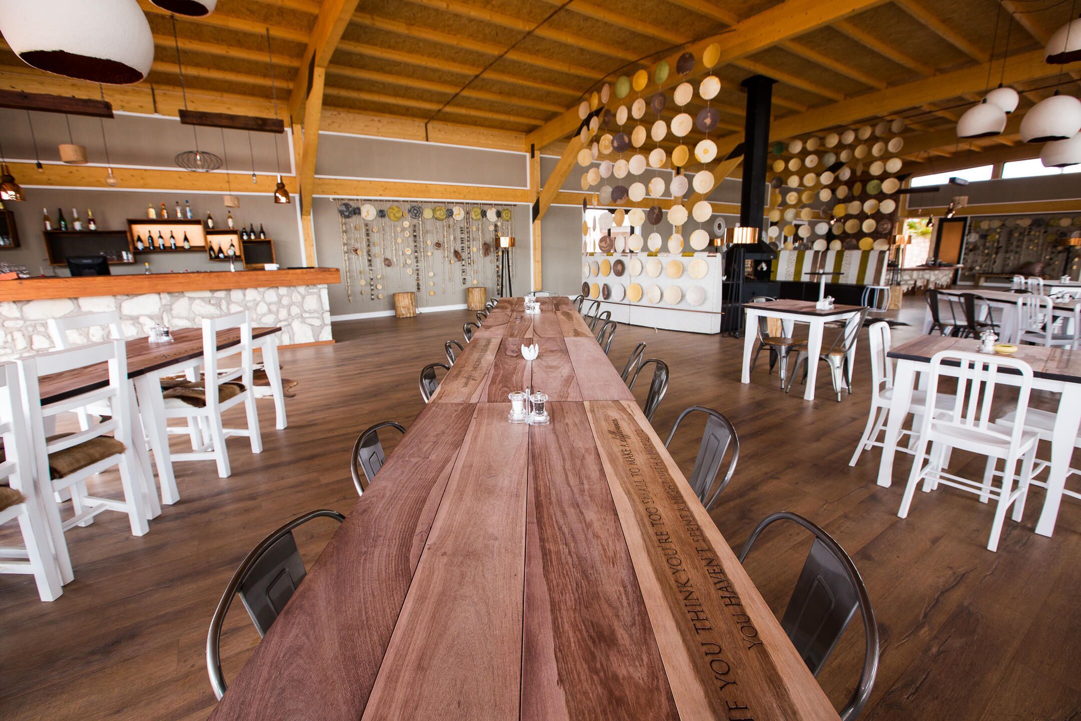 A spacious dining area with a long wooden table, white chairs, and a bar area with wine bottles.