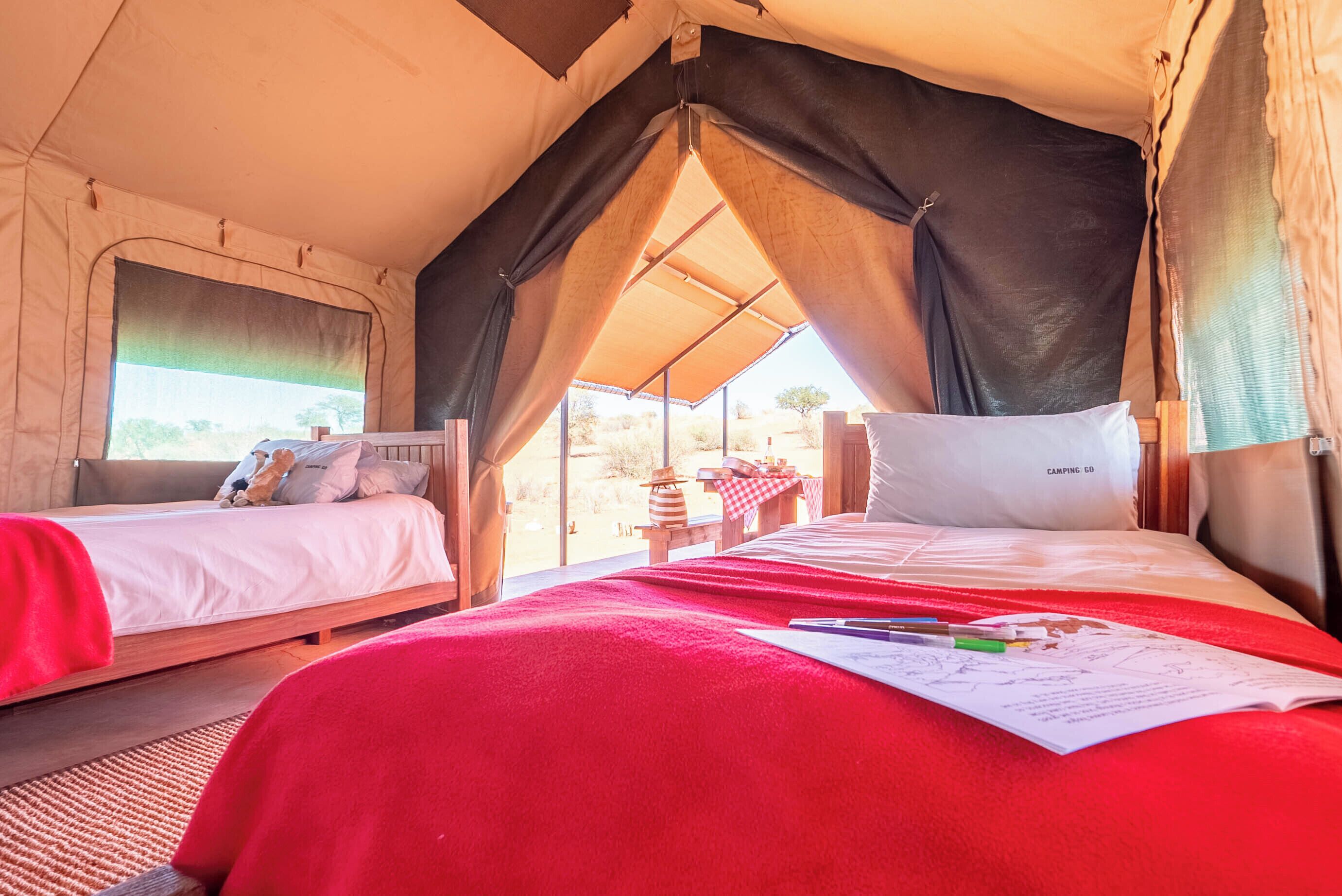 A tent with two beds, one with a red blanket and the other with a white blanket.