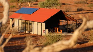 Un edificio con techo rojo y paneles solares, rodeado de vegetación seca y árboles.