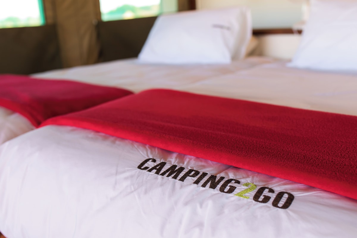 A bed with white bedding and a red blanket, and the text "CAMPING2GO" on the pillow.