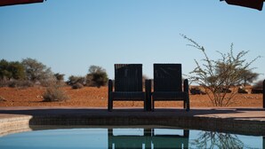 Dos sillones de mimbre mirando a una piscina, con cielo despejado y vegetación escasa al fondo.