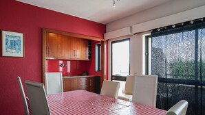 A dining area with a red and white checkered tablecloth, wooden cabinets, and a view through a patterned curtain. - Selway Green Apartment, Wifi, Swimming Pool !New! (Quarteira)
