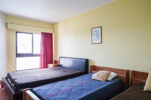 Ein Zimmer mit zwei Betten, einem Fenster mit roten Vorhängen und einem gerahmten Bild an der Wand.