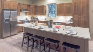 Une cuisine moderne avec des meubles en bois, un réfrigérateur en acier inoxydable, un îlot central doté de tabourets de bar et une fenêtre donnant sur un espace verdoyant.