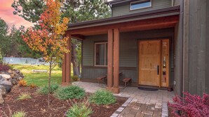 Une maison moderne dotée d’un porche abrité, d’une porte en bois et d’un petit jardin où poussent différentes espèces de plantes.