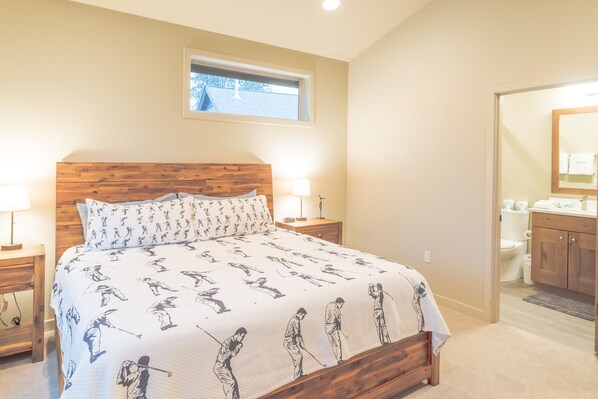 Een slaapkamer met een houten hoofdbord, een groot bed met een beddekleed met patroon, twee nachtkastjes met lampen, en een raam boven het bed.