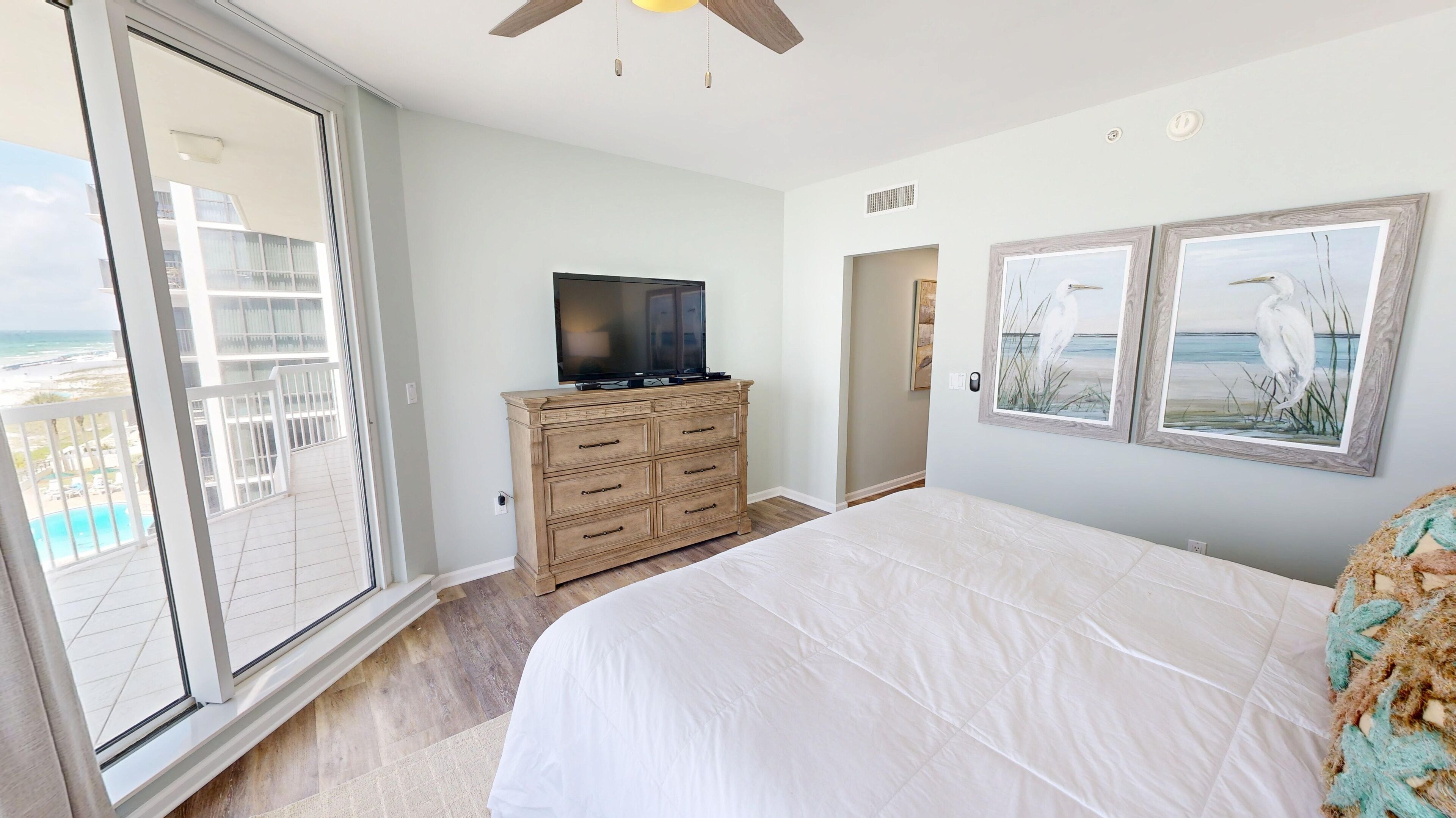 Un dormitorio con una cama grande, un aparador de madera, un televisor de pantalla plana y un balcón con vista a la playa.