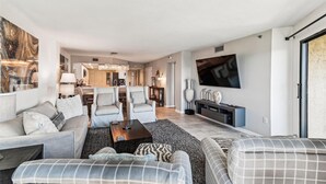 A spacious living room with a large TV, comfortable seating, and a dining area in the background. - IR 518 is a Stunning 2 BR that has amazing Sunset views - sleeps 10 by RedAwning (Destin)