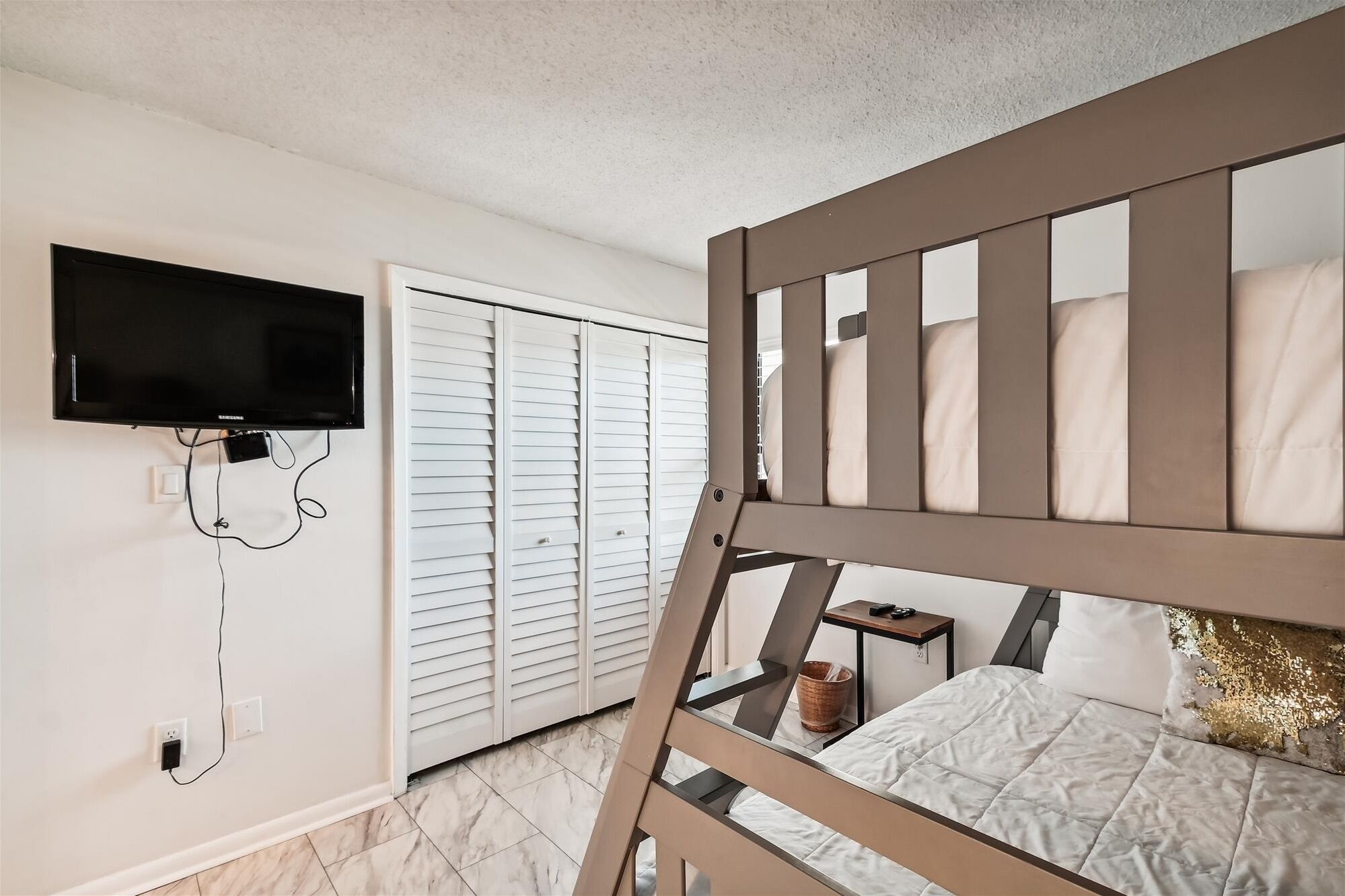 A bedroom with a bunk bed, a television mounted on the wall, and a window with blinds.