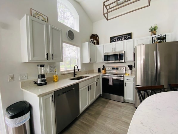 Kitchen features white cabinetry, stainless steel appliances, and a large window, with a well-organized layout including a dishwasher, sink, and oven.