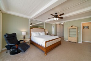 Een slaapkamer met een groot bed, een stoel, een nachtkastje, een lamp, een plafondventilator, een spiegel en een garderobe.