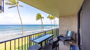 A balcony with a view of the ocean and palm trees. There are two tables and four chairs. - Papakea L-301  Direct Oceanfront Corner Unit with Panoramic Views (Lahaina)