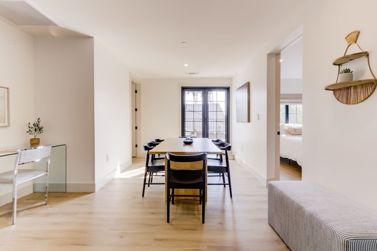 A modern dining area with a wooden table and chairs, a bench, and a wall-mounted shelf with a plant.