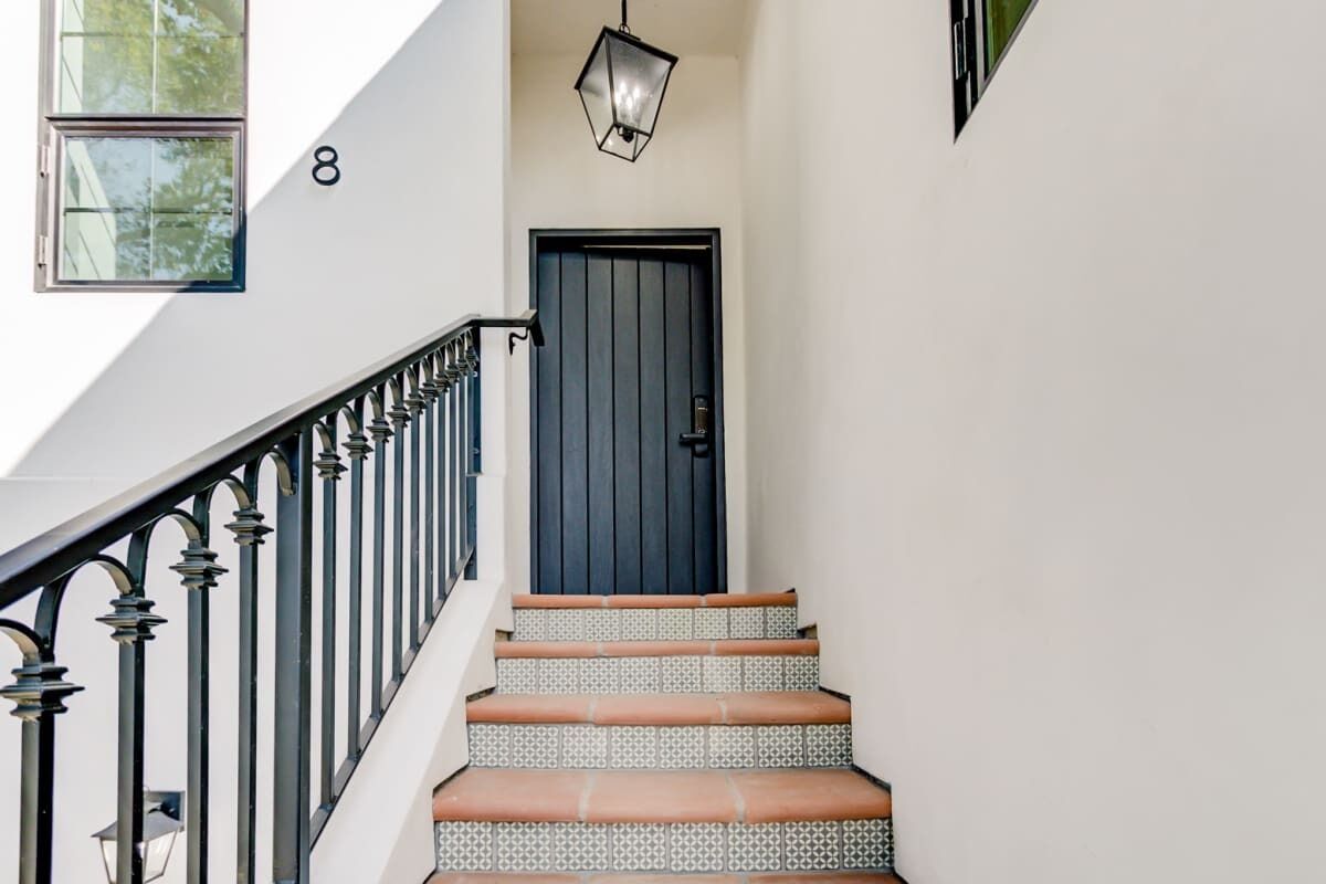 A staircase with patterned steps leading to a dark door, a black railing, and a hanging light fixture.