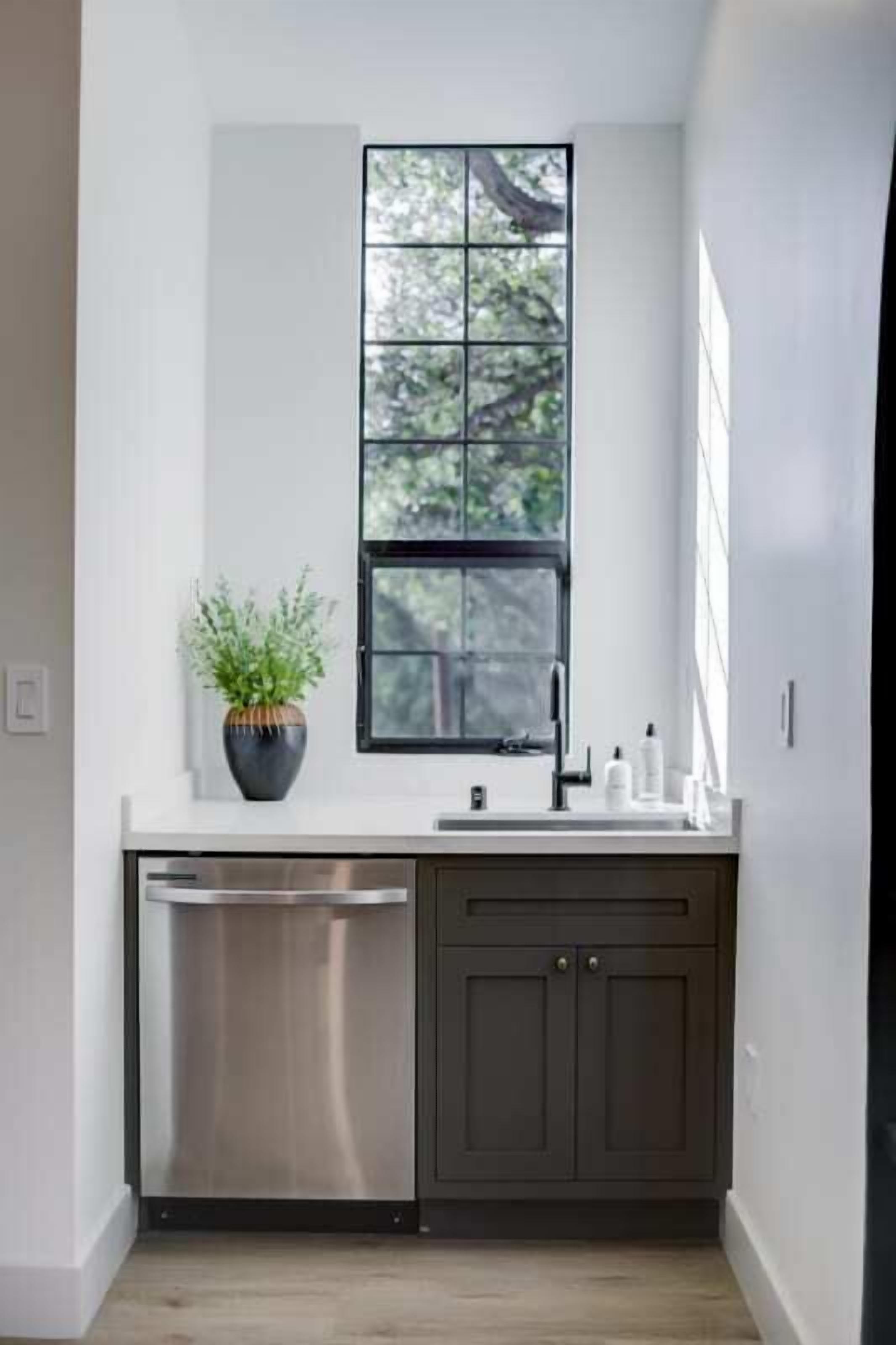 A modern kitchen with a built-in dishwasher, a window above the sink, and a potted plant on the countertop.