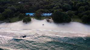 An aerial view of a beach with a large house surrounded by trees.
