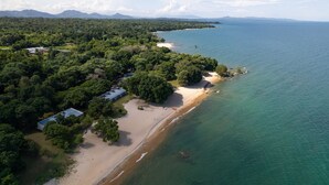 An aerial view of a coastal area with a beach, dense greenery, and a few buildings. - Sunbird Chintheche Inn (Chintheche)