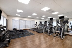 Une salle de sport équipée de tapis de course, de vélos elliptiques et d’un piano.