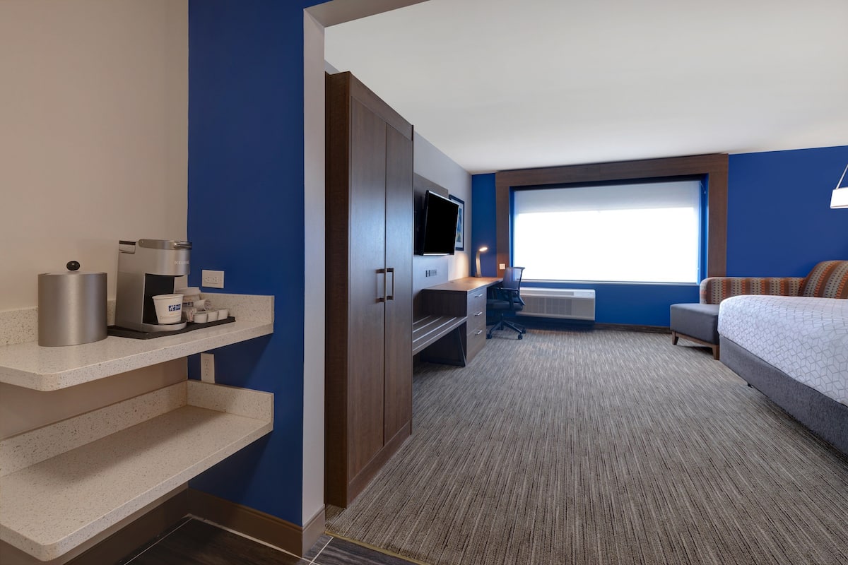 Ett hotellrum med ett skrivbord, en säng, en TV och ett fönster.