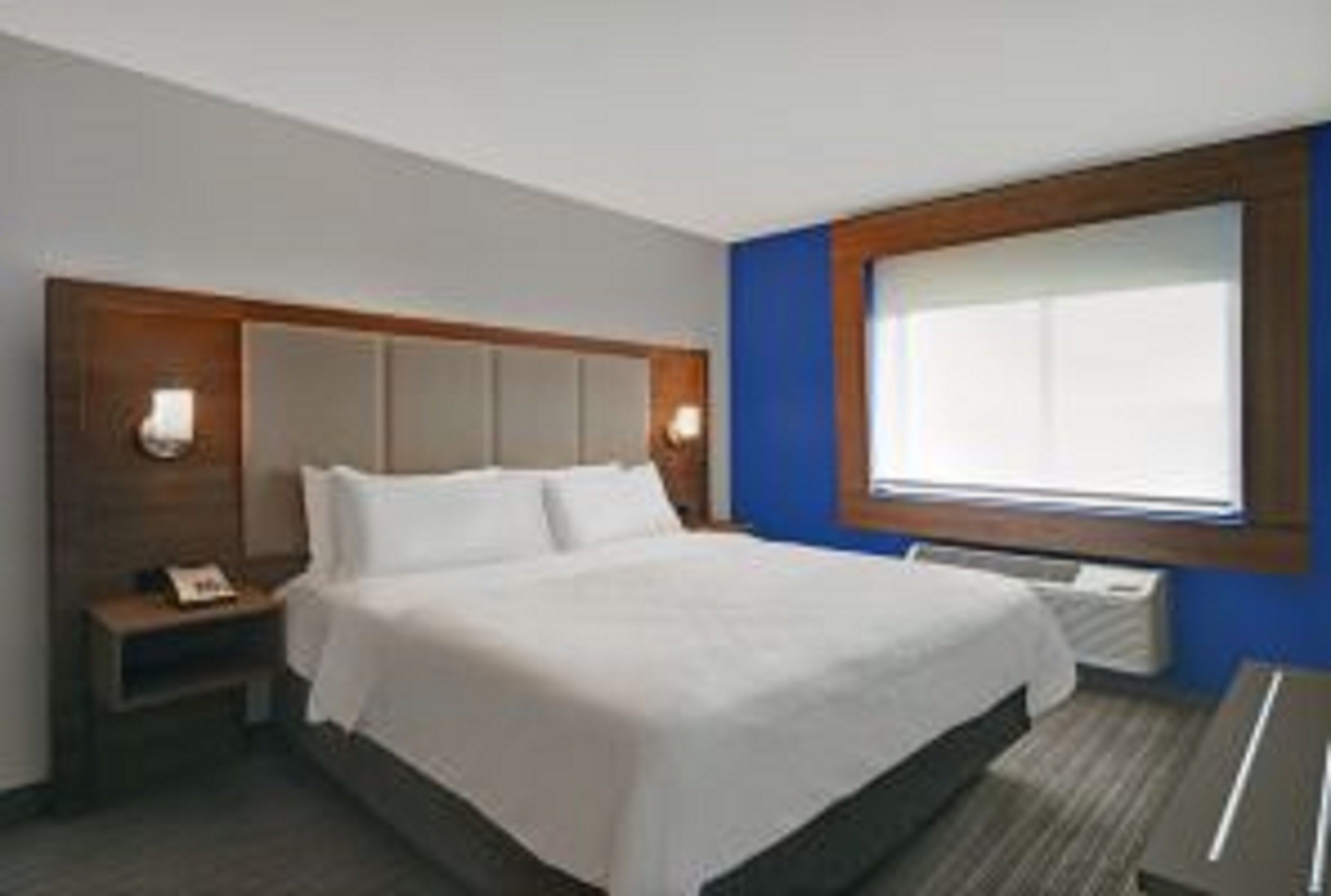 Une chambre d’hôtel avec un lit, une table de chevet, une fenêtre et un luminaire fixé au mur.