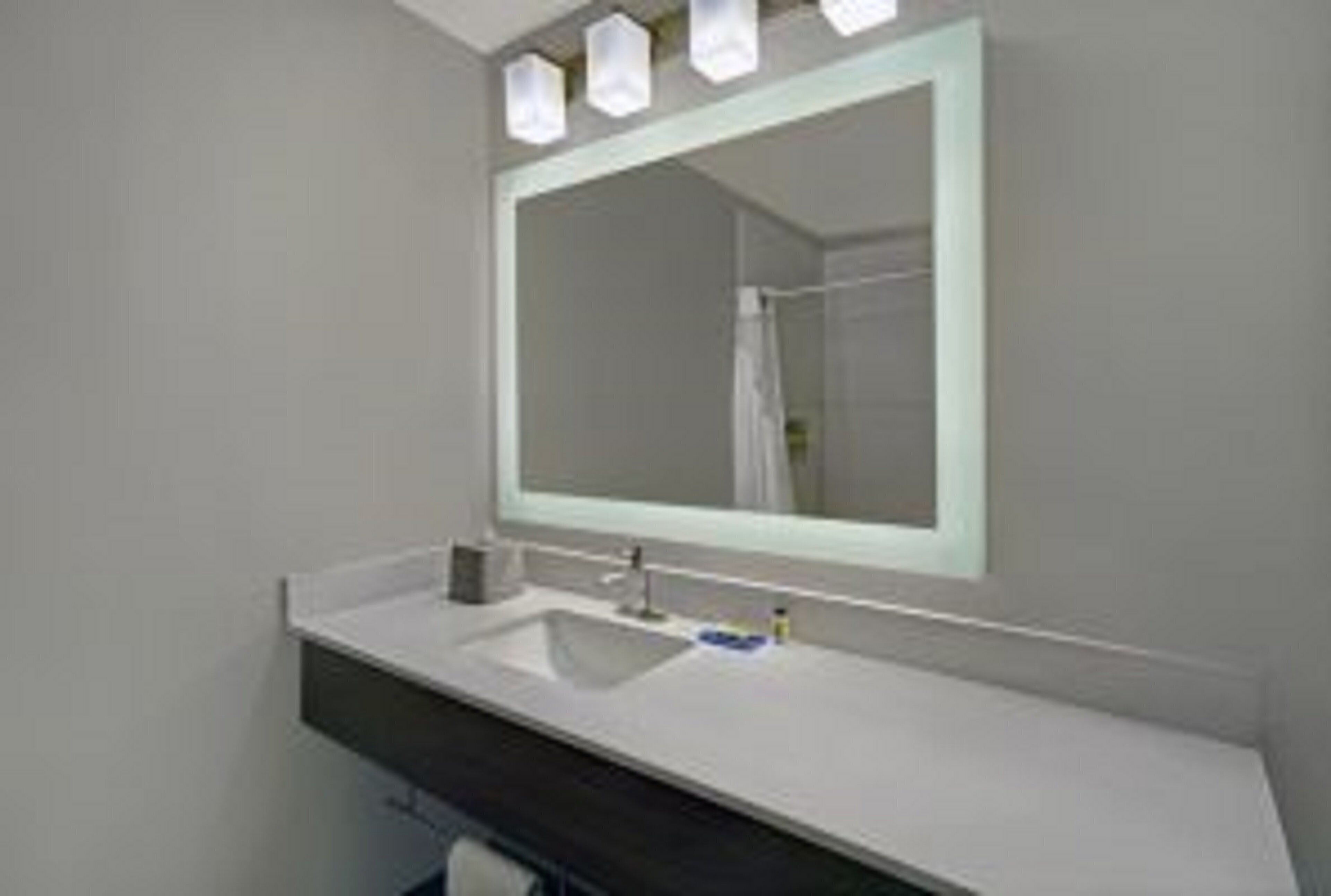 Un baño con un lavabo blanco, un espejo y una ducha visible en el reflejo.