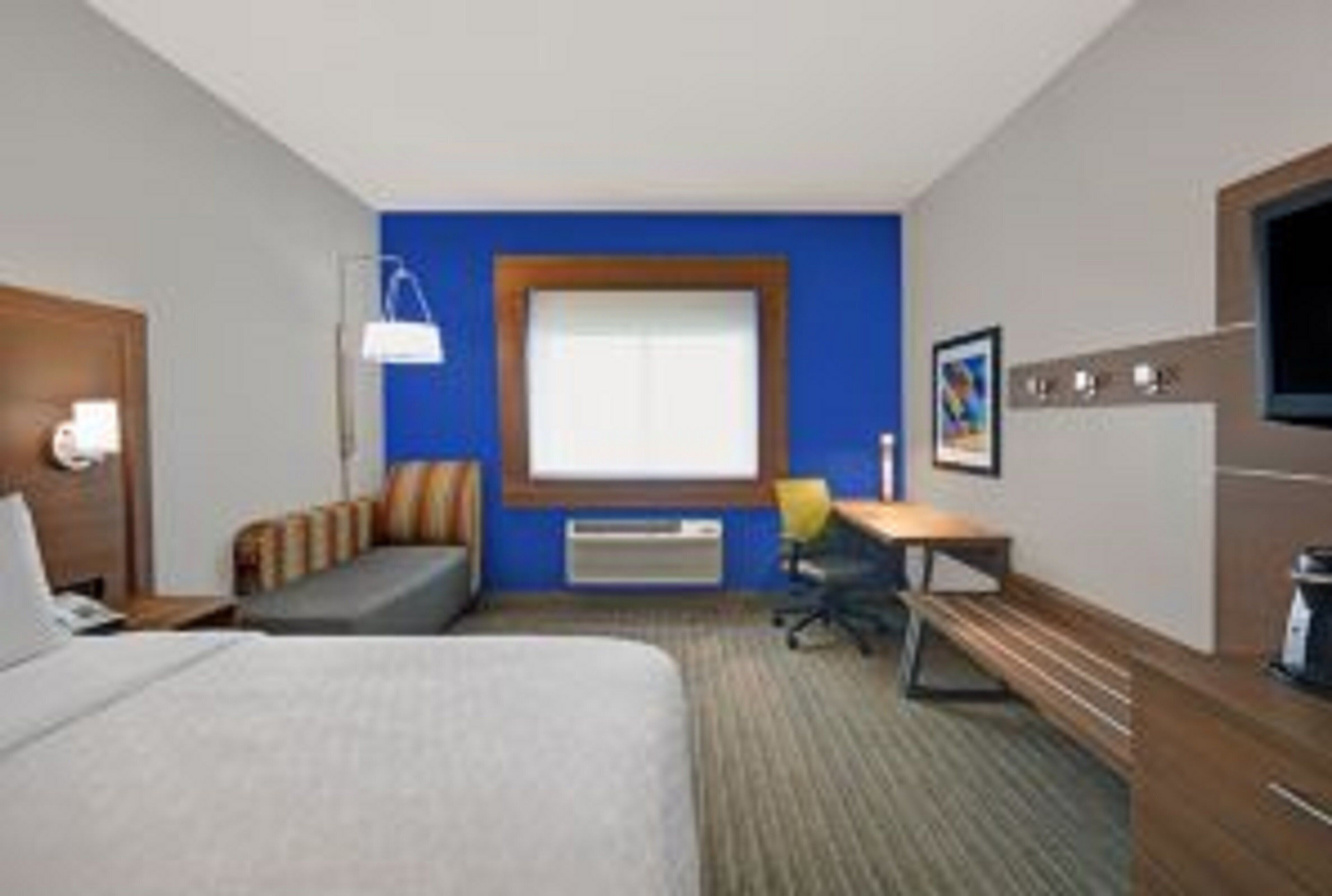 A hotel room with a bed, a desk, a chair, a window, and a wall-mounted TV.