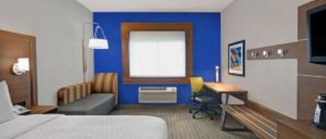 A hotel room with a bed, a desk, a chair, a window, and a wall-mounted TV.