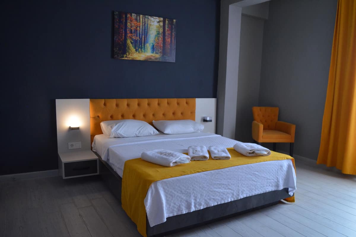 A hotel room with a large bed, a nightstand, a chair, and a painting on the wall.