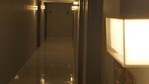 Un largo pasillo tenuemente iluminado con varias puertas y una lámpara en la pared.