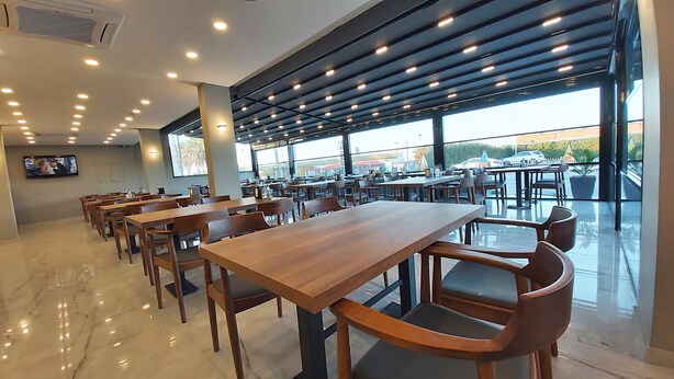 Un amplio comedor interior con varias mesas y sillas de madera, ventanas grandes que ofrecen vistas al exterior y un televisor de pantalla plana montado en la pared.