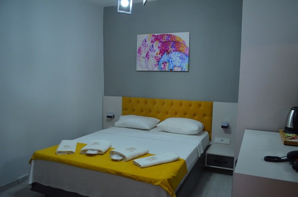 Habitación de hotel con cama, cabecera amarilla, almohadas blancas y un cuadro en la pared.