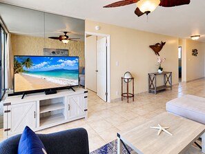 Een woonkamer met een flatscreen televisie op een kast, een plafondventilator, een deur, een klein tafeltje met een wereldbol en een decoratief object aan de muur.
