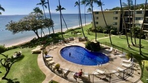 A pool area with a view of the ocean, surrounded by palm trees and a building. - Where Blue Waters Beckon Maalaea Remodeled 2BR Condo Ocean Views Harbor (Maalaea)