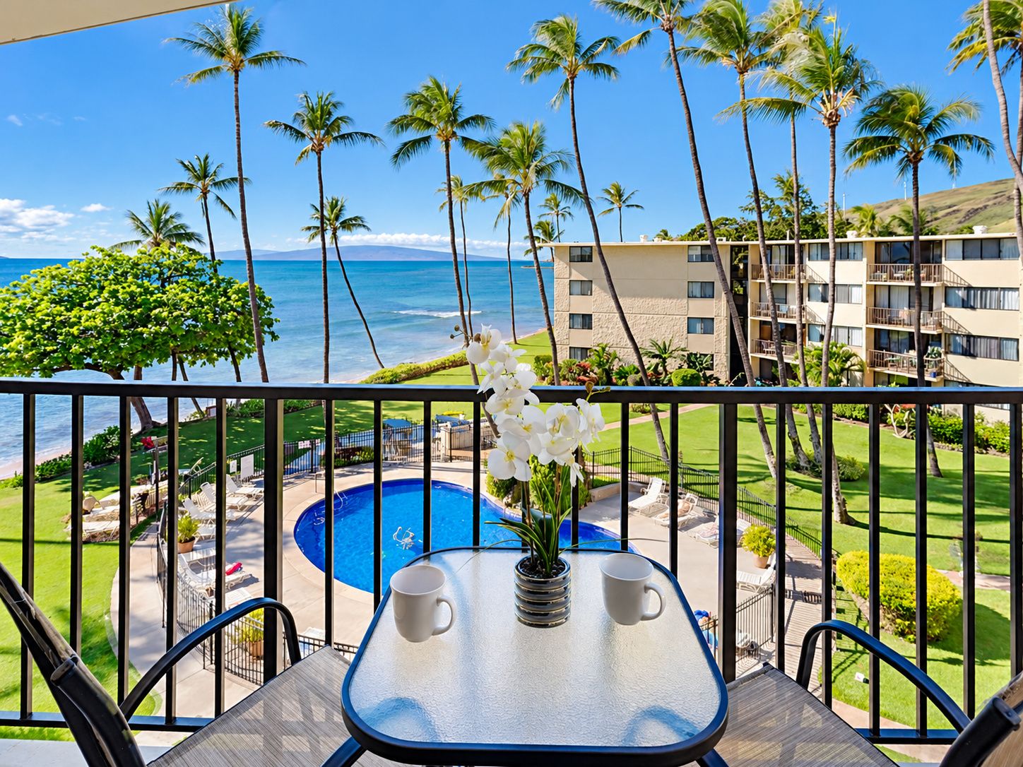 A balcony with a view of the ocean, a pool, and a building with multiple floors.