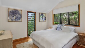 A bedroom with a large bed, a ceiling fan, and a window with a view of greenery. - Large, pets welcome family home close to beaches, shops and public transport. (Point Lookout)