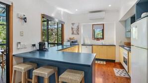 A modern kitchen with a blue island, yellow cabinets, and a view of greenery outside. - Large, pets welcome family home close to beaches, shops and public transport. (Point Lookout)