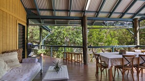 A covered outdoor seating area with a wooden deck, a sofa, and a table with chairs. - Large, pets welcome family home close to beaches, shops and public transport. (Point Lookout)