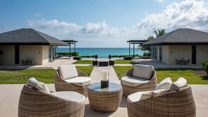 Ein Strandgrundstück mit zwei überdachten Bereichen, einem zentralen Sitzbereich mit Rattanmöbeln und Blick aufs Meer.