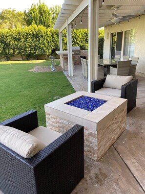 An outdoor patio area with a stone fire pit, wicker furniture, and a covered seating area with a table and chairs.