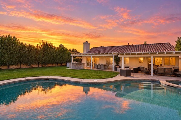 A house with a swimming pool, a covered patio, and a view of the sunset.