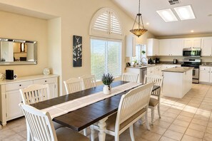 A modern kitchen with white cabinetry, a central island, and a dining area with a dark wood table and white chairs.
