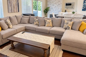A living room with a sectional sofa, a coffee table, and a dining area with a white table and chairs.