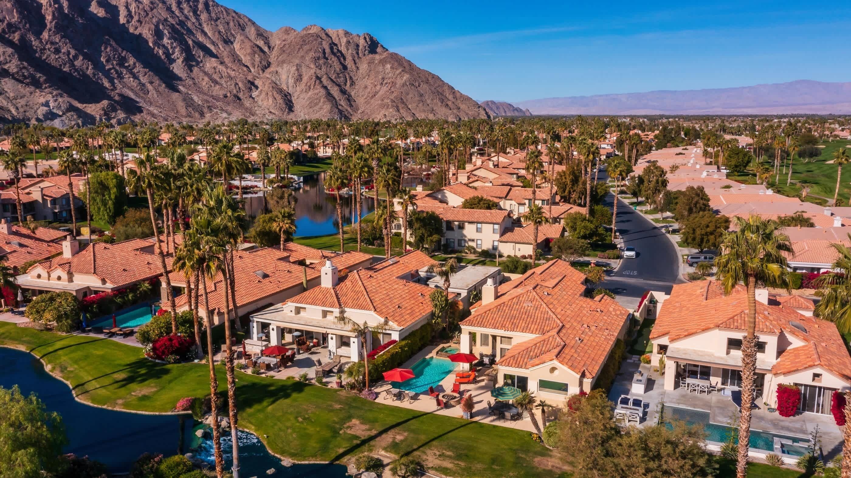 Un barrio residencial con casas de techo rojo, palmeras y una gran montaña al fondo.