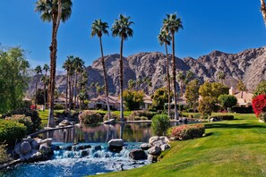 Un resort con piscina, palmeras y montañas al fondo.
