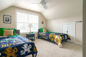A bedroom with two beds, a ceiling fan, a window with blinds, and a door.