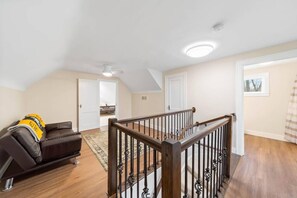 Ein geräumiger Wohnbereich mit Holztreppe, einem schwarzen Ledersofa und Blick auf das angrenzende Schlafzimmer.