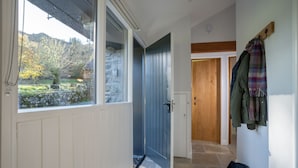 A hallway with a stone wall, a blue door, and a coat rack with jackets. - Grasmere Cottage with Stunning Views by LetMeStay (Ambleside)