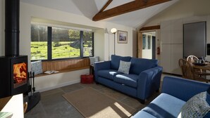 A cozy living room with a blue sofa, a wooden bench, and a black wood stove. - Grasmere Cottage with Stunning Views by LetMeStay (Ambleside)